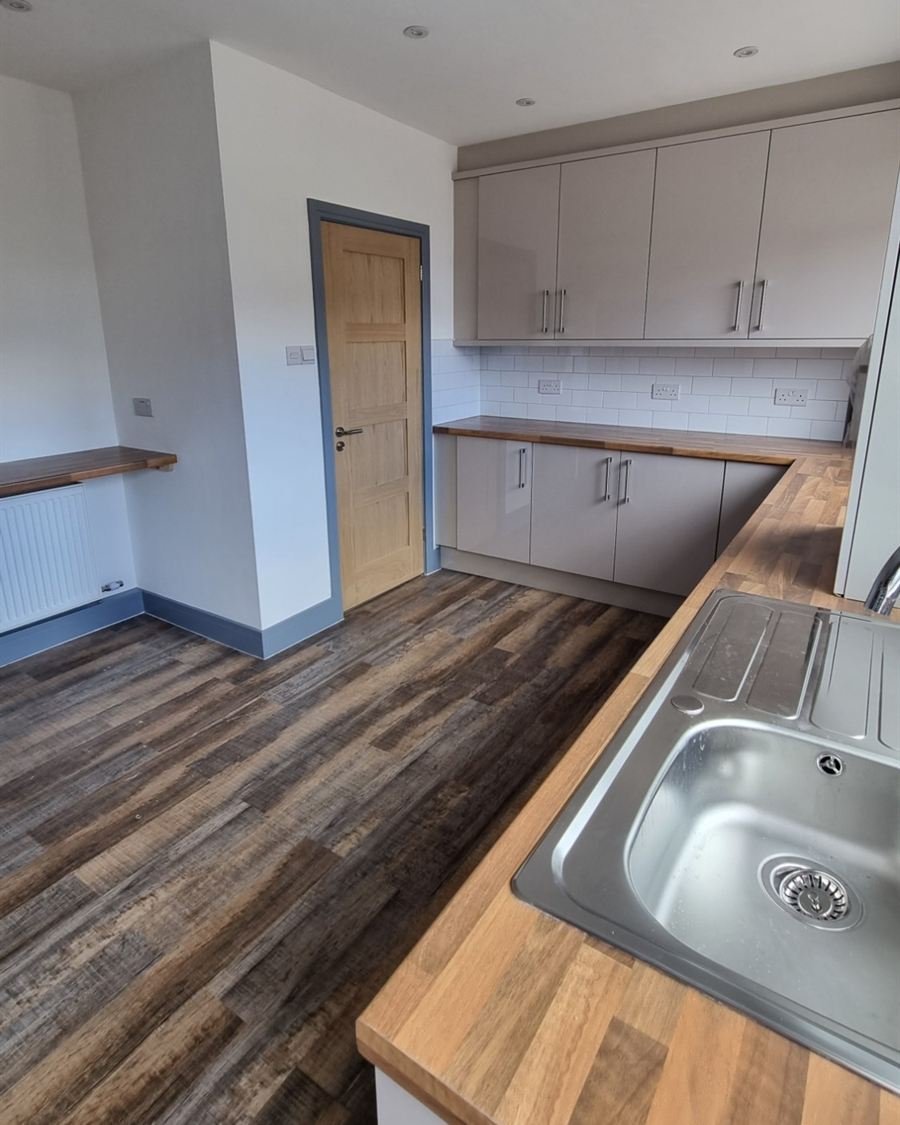 The same kitchen after: new grey gloss units, wood worktops, an oak door and new flooring