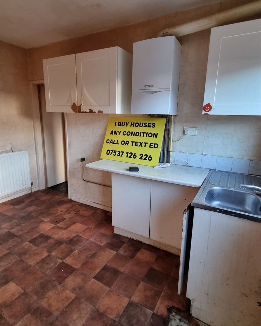 The kitchen before: peeling cupboards, stained floor, and Ed's yellow sign on the worktop